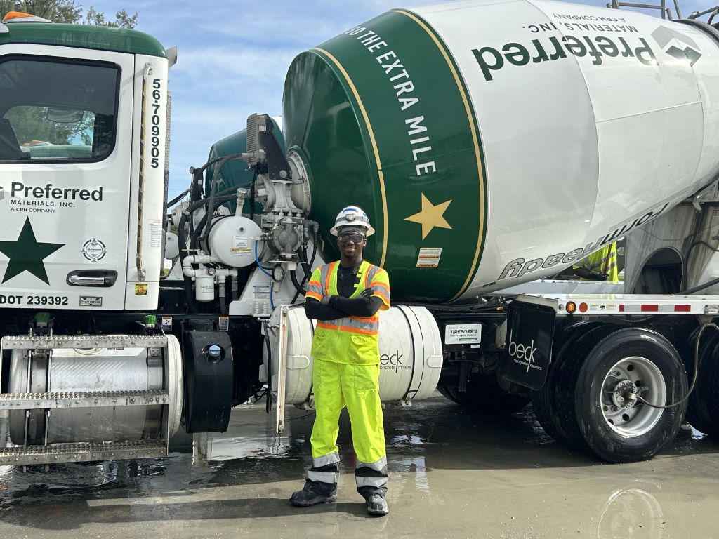 A man stands beside a cement truck mixer, ready to pour concrete at a construction site